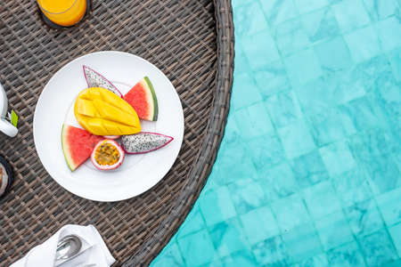 Floating Breakfast tray in swimming pool at luxury hotel or tropical resort villa, fruits; mango, watermelon dragon fruit, passion fruit and orange juice. Exotic summer travel and healthy food conceptの写真素材