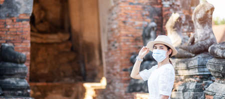 Tourist Woman in white dress wearing surgical face mask, protection COVID-19 pandemic during visiting in Wat Chaiwatthanaram temple in Ayutthaya. new normal, safety travel and Thailand travel conceptの写真素材