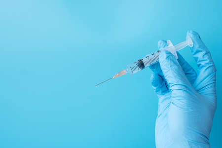 Hand of doctor injection vaccine or drug by Needle Syringe on blue background in hospital...