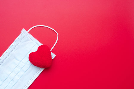 heart shape decoration and Medical face mask on red background against Coronavirus disease infection. Love, together and Happy Valentines day under Covid-19 pandemic conceptの写真素材