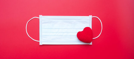 heart shape decoration and Medical face mask on red background against Coronavirus disease infection. Love, together and Happy Valentines day under Covid-19 pandemic conceptの写真素材