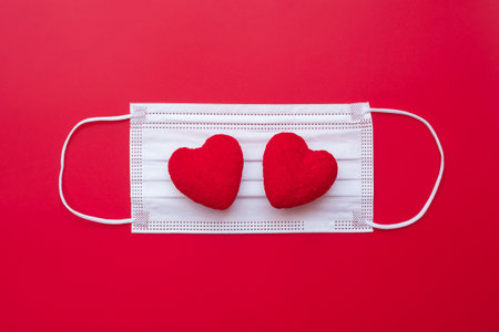 heart shape decoration and Medical face mask on red background against Coronavirus disease...