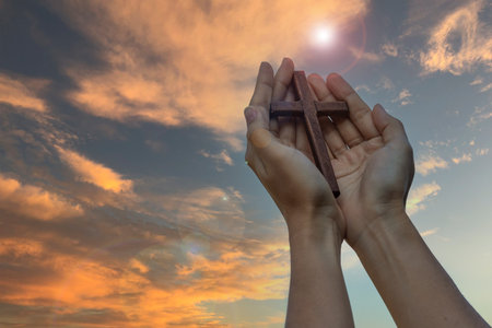 Hand holding wood cross against sunrise background, open palm up worship, pray for blessings from God. Christian Religion, Crucifix and Faith conceptの写真素材