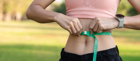 Young slim body female in pink sportswear, healthy woman measuring her thin waist with a tape...