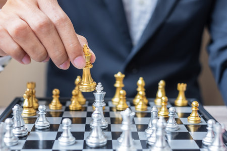 businessman hand moving gold Chess King figure and Checkmate enermy or opponent during chessboard competition. Strategy, Success, management, business planning, interruption and leadership conceptの写真素材