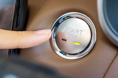 Finger press a car ignition button or START engine inside modern electric automobile. Keyless,...