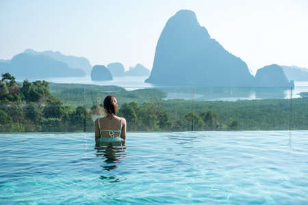 Happy woman in white swimsuit swimming in luxury pool hotel against Phang Nga bay background, Tourist relaxing at Samet Nang She, near Phuket in Southern Thailand. travel, trip and summer vacationの写真素材