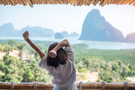 happy woman in bathrobe stretching after waking up and enjoy Phang Nga bay view point, Tourist relaxing in tropical resort at Samet Nang She, near Phuket in Thailand. Travel summer vacation conceptの写真素材