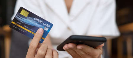 Businesswoman holding credit card and using touchscreen smartphone for online shopping while making...