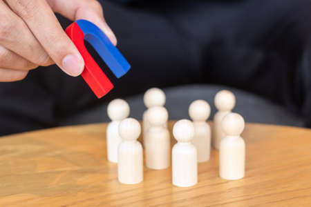 Businessman hand holding magnet and pulling man wooden figure from the crowd employee. Business, Human resource management, Recruitment, Teamwork, strategy, toxic people and leadership Conceptsの写真素材