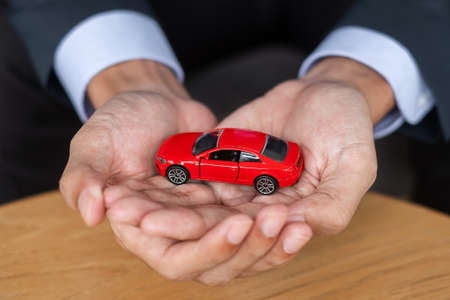 Businessman hand holding red car toy on table. Financial, money, refinance and Car insurance conceptの写真素材