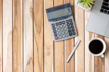 Top view Office desk with calculator, pen, computer laptop, plant pot and coffee cup on wood tableの写真素材