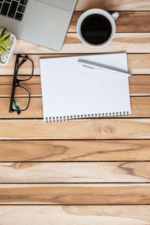 Top view Office desk with pen, computer laptop, blank notebook, plant pot and coffee cup on wood table background. workspace or home office with copy space for text conceptの写真素材