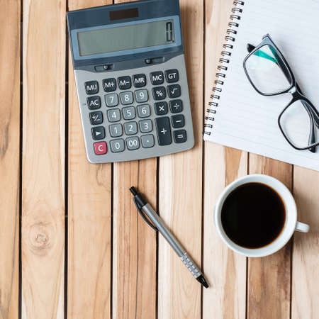 Top view Office desk with calculator, pen, eyeglasses, blank notebook and coffee cup on wood table background. workspace or home office with copy space for text conceptの写真素材
