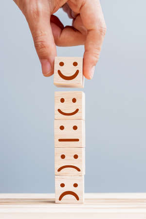 Hand holding smile face symbol on wooden cube blocks. Emotion, Service rating, ranking, customer review, satisfaction and feedback conceptの写真素材