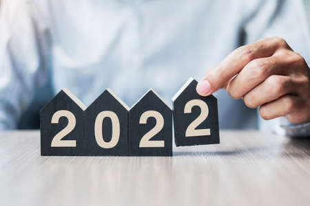 Businessman hands holding 2022 Happy New Year with house model on table office.