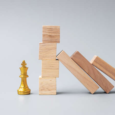 Wooden Blocks or Dominoes falling to golden Chess King figure.の写真素材