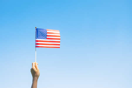 hand holding United States of America flag on blue sky background. USA holiday of Veterans,...