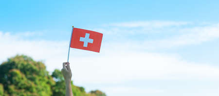 hand holding Switzerland flag on blue sky background. Switzerland National Day and happy celebration conceptsの写真素材