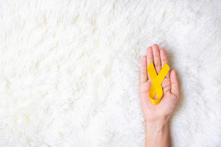 hand holding Yellow Ribbon on white background for supporting people living and illness. September Suicide prevention day, Childhood Cancer Awareness month and World cancer day conceptの写真素材
