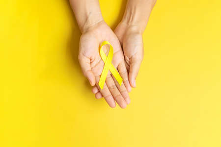 hand holding Yellow Ribbon on yellow background for supporting people living and illness. September...