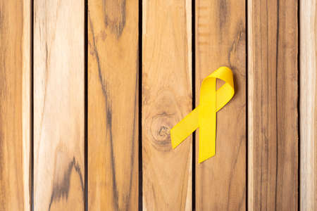 Yellow Ribbon on wooden table background for supporting people living and illness. September Suicide prevention day, Childhood Cancer Awareness month and World cancer day conceptの写真素材