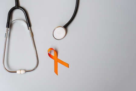Leukemia, Kidney cancer day, world Multiple Sclerosis, CRPS, Self Injury Awareness month, Orange Ribbon with stethoscope for support people living and illness. Healthcare and World cancer day conceptの写真素材