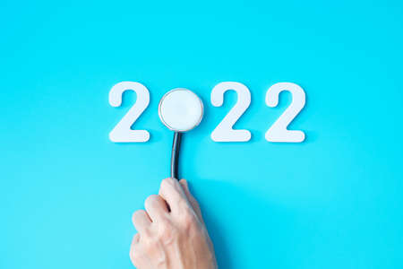 hand holding Stethoscope with 2022 number on blue background. Happy New Year for healthcare, Insurance, Wellness and medical conceptの写真素材