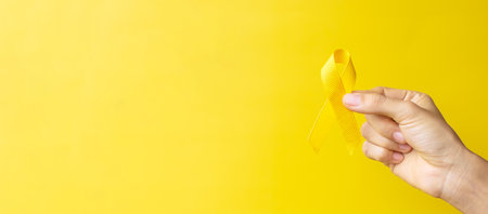 hand showing Yellow Ribbon on yellow background for supporting people living and illness. September...