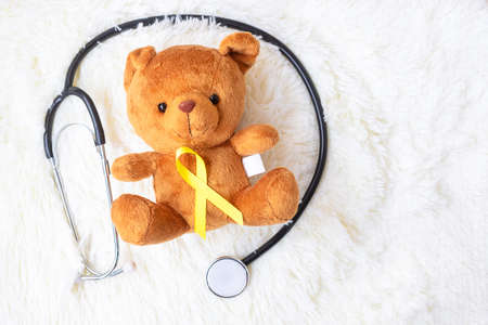 Yellow Ribbon on Bear doll with stethoscope on white background for supporting kid living and...