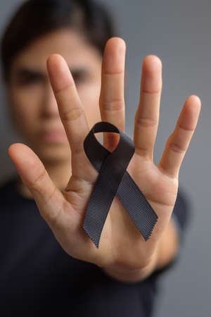 Woman holding black Ribbon for Melanoma and skin cancer, Vaccine injury awareness month, grief and rest in peace. Healthcare and Racist conceptの写真素材