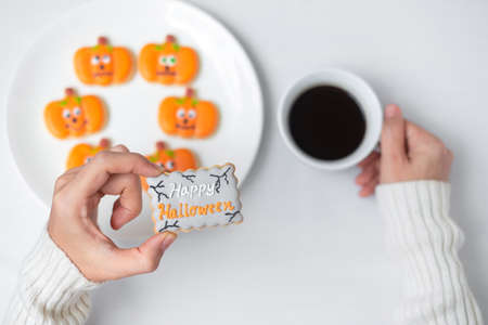 woman hand holding funny Halloween Cookie during drinking coffee. Happy Halloween day, Trick or Threat, Hello October, fall autumn, Traditional, party and holiday conceptの写真素材