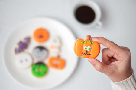 woman hand holding funny Halloween Cookie during drinking coffee. Happy Halloween day, Trick or Threat, Hello October, fall autumn, Traditional, party and holiday conceptの写真素材