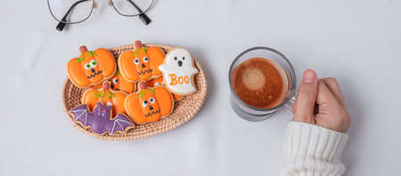 woman hand holding coffee cup during eating funny Halloween Cookies. Happy Halloween day, Trick or Threat, Hello October, fall autumn, Traditional, party and holiday conceptの写真素材
