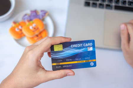 Hand holding credit card for online shopping on laptop during eating Halloween Cookies and coffee. Happy Halloween, Hello October, fall autumn, Festive, party and holiday conceptの写真素材