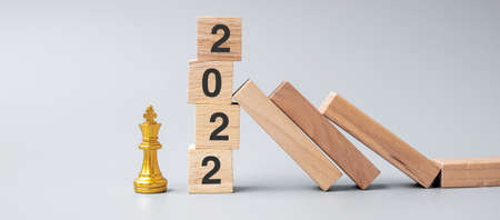 wooden Dominoes falling against 2022 stop blocks with golden Chess King figure. Business, Risk Management, Solution, economic, Insurance and New Year conceptの写真素材