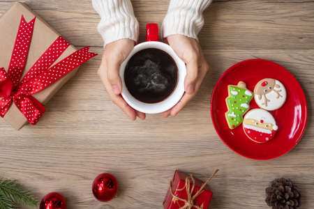 Merry Christmas with woman hand holding coffee cup and homemade cookie on table. Xmas eve, party,...