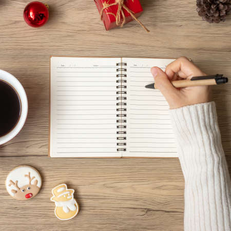Woman hand writing on notebook with black coffee cup and Christmas cookies on table. Xmas, Happy New Year, Goals, Resolution, To do list, Strategy and Plan conceptの写真素材