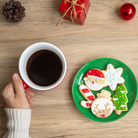 Merry Christmas with woman hand holding coffee cup and homemade cookie on table. Xmas eve, party, holiday and happy New Year conceptの写真素材