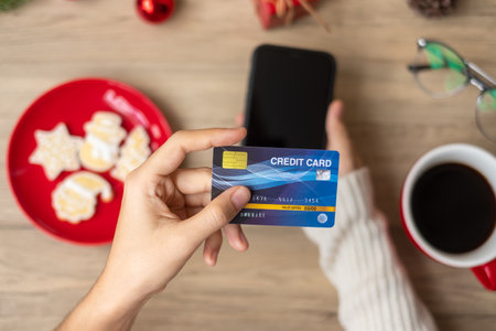 Hand holding credit card for online shopping on smartphone during eating Homemade Xmas Cookies and coffee. Merry Christmas eve, December, seasonal, Black Friday sale, New Year and holiday conceptの写真素材