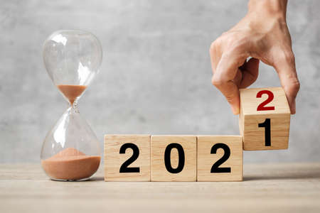 hand flipping block 2021 to 2022 text with hourglass on table. Resolution, time, plan, goal, motivation, reboot, countdown  and New Year holiday conceptsの写真素材