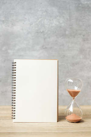 Hourglass with Blank notebook on table, Sand flowing through the bulb of Sandglass measuring the passing. countdown, deadline, Life time and Retirement conceptの写真素材