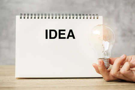 Hand holding lightbulb over notebook on table. New Ideas, Creative, Innovation, Imagination, inspiration, Resolution, Strategy and goal conceptの写真素材