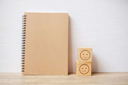 emotion face block and notebook on table. Emoticon for customer review, satisfaction, mood, mental health and feedback conceptの写真素材