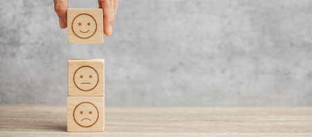 hand holding emotion face block. Customer choose Emoticon for user reviews. Service rating, ranking, customer review, satisfaction, mood, evaluation and feedback conceptの写真素材