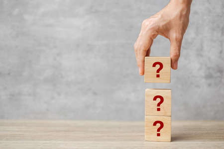hand holding Questions Mark ( ? ) on cube block on table. FAQ( frequency asked questions), Answer, Q and A, Information, Communication and interrogation Conceptsの写真素材