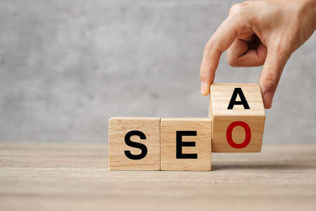 Hand flip SEA to SEO text wooden cube blocks on table background. Search Engine Optimization, Advertising, Idea, Strategy, marketing, Keyword and Content conceptの写真素材