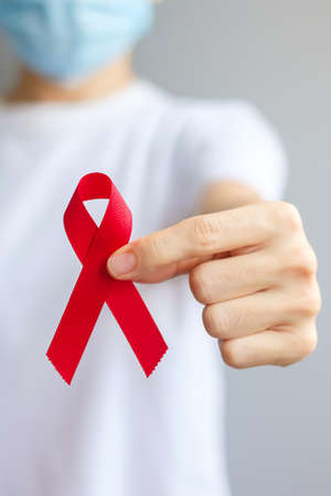 Hand holding Red Ribbon for December World Aids Day (acquired immune deficiency syndrome), multiple myeloma Cancer Awareness month and National Red ribbon week. Healthcare and world cancer day conceptの写真素材