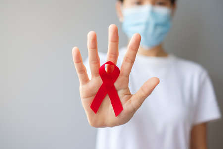 Hand holding Red Ribbon for December World Aids Day (acquired immune deficiency syndrome), multiple myeloma Cancer Awareness month and National Red ribbon week. Healthcare and world cancer day conceptの写真素材