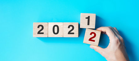 hand holding wooden cube block with 2022 text on blue background. Resolution, plan, review, goal, start and New Year holiday conceptsの写真素材